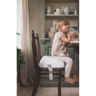 Petite fille assise sur le rehausseur de chaise Babybjorn.